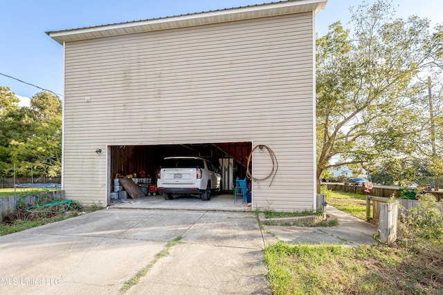 garage with driveway, a trampoline, and fence
