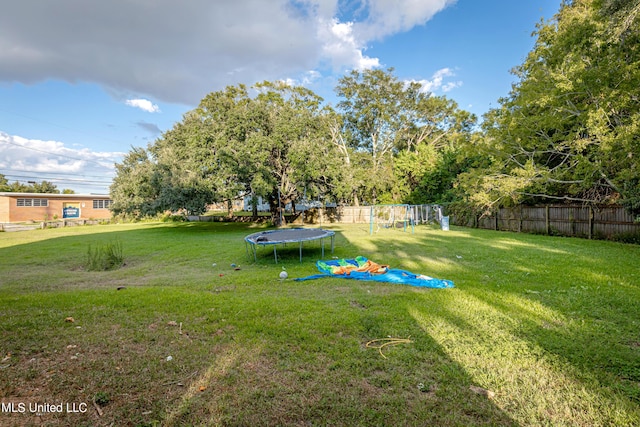 view of yard featuring a trampoline, fence, and a playground