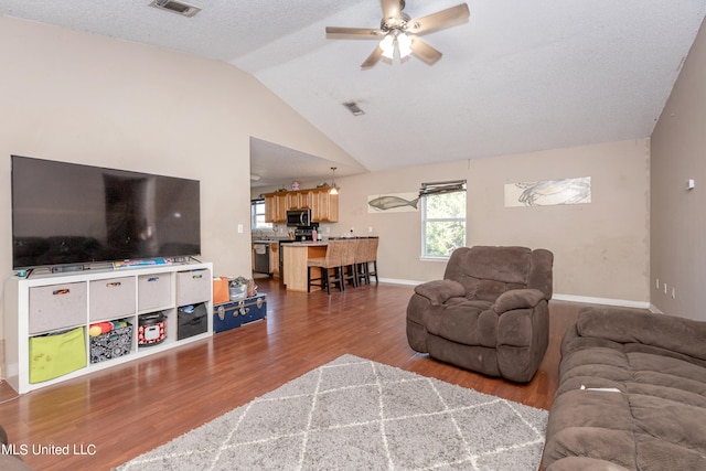 living room with ceiling fan, hardwood / wood-style flooring, a textured ceiling, and lofted ceiling