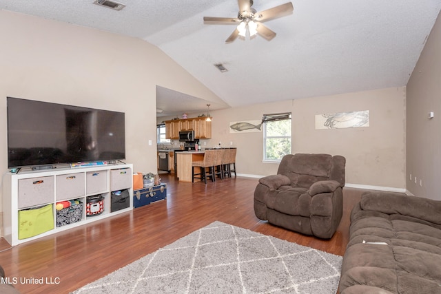 living area featuring wood finished floors, a ceiling fan, visible vents, baseboards, and lofted ceiling