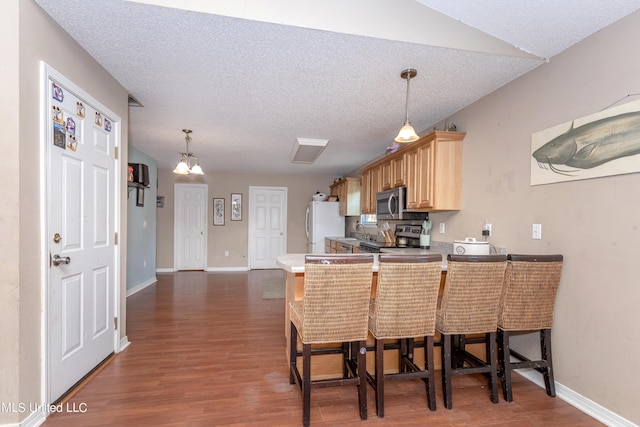 kitchen featuring dark wood-style flooring, stainless steel appliances, light brown cabinets, a peninsula, and baseboards