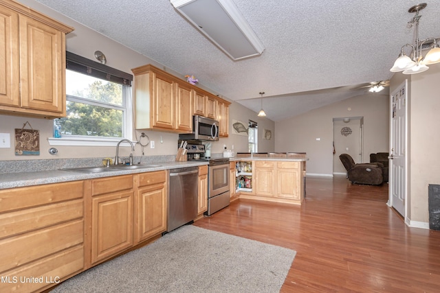 kitchen featuring wood finished floors, stainless steel appliances, a textured ceiling, a sink, and a peninsula