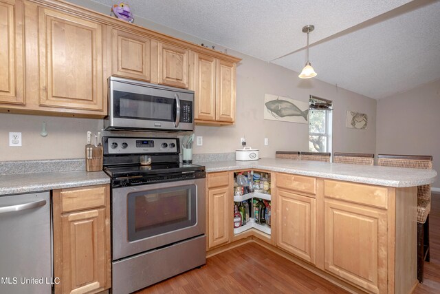kitchen with appliances with stainless steel finishes, light wood finished floors, a peninsula, and light brown cabinetry