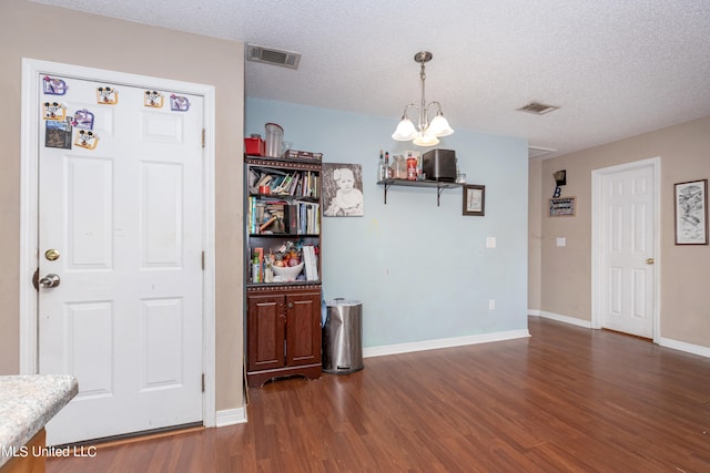 unfurnished dining area with dark wood-type flooring, a notable chandelier, and a textured ceiling