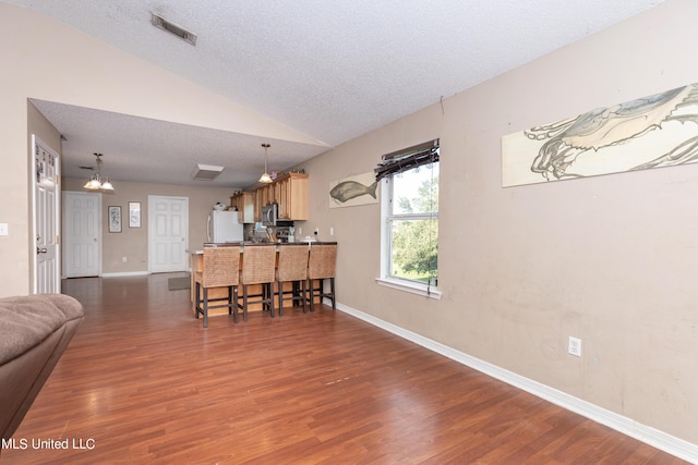 living area featuring visible vents, vaulted ceiling, baseboards, a textured ceiling, and wood finished floors