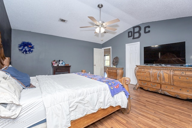 bedroom with vaulted ceiling, a textured ceiling, light hardwood / wood-style floors, and ceiling fan