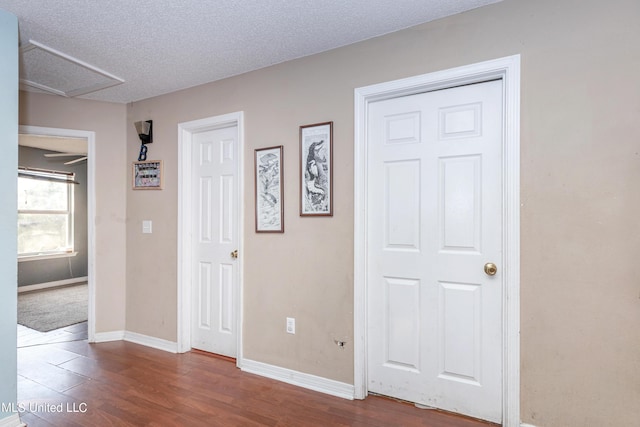 hallway featuring attic access, dark wood-style floors, a textured ceiling, and baseboards