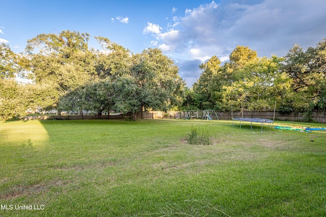 view of yard featuring a trampoline, a fenced backyard, and playground community