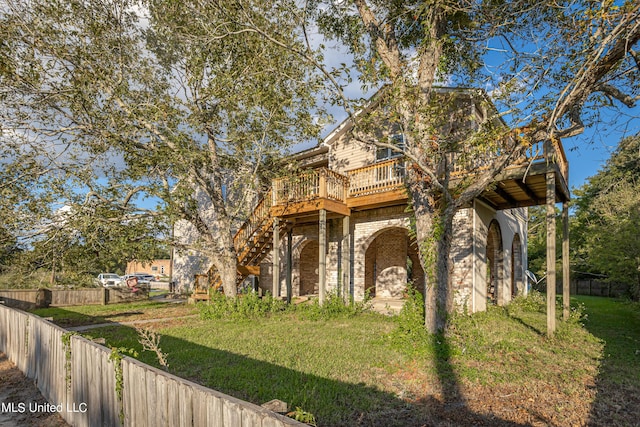 view of front of property with brick siding, fence, a wooden deck, a front yard, and stairs