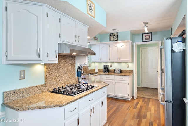 kitchen with white cabinets, light hardwood / wood-style flooring, stainless steel fridge, light stone counters, and gas cooktop