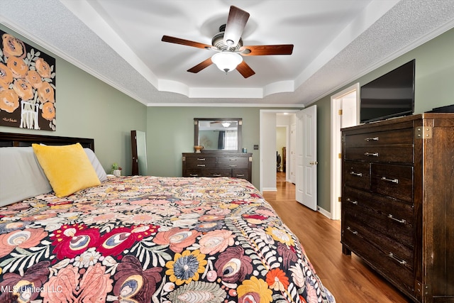 bedroom featuring a tray ceiling, ceiling fan, ornamental molding, and light wood-type flooring