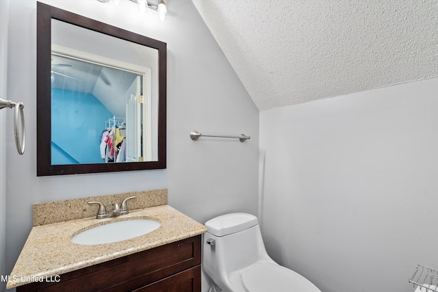 bathroom featuring a textured ceiling, vanity, vaulted ceiling, and toilet