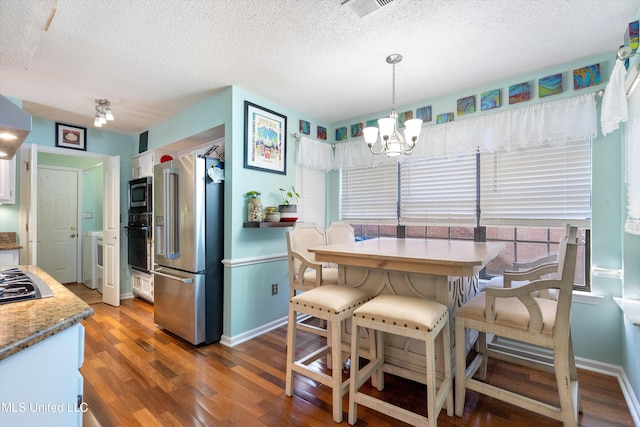 interior space featuring dark wood-type flooring, white cabinets, a textured ceiling, appliances with stainless steel finishes, and a chandelier