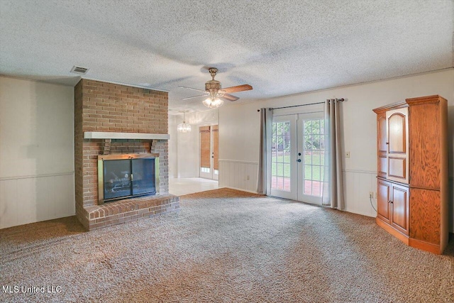 unfurnished living room featuring french doors, a brick fireplace, a textured ceiling, carpet flooring, and ceiling fan