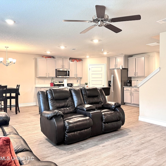 living room featuring a textured ceiling, light hardwood / wood-style floors, and ceiling fan with notable chandelier