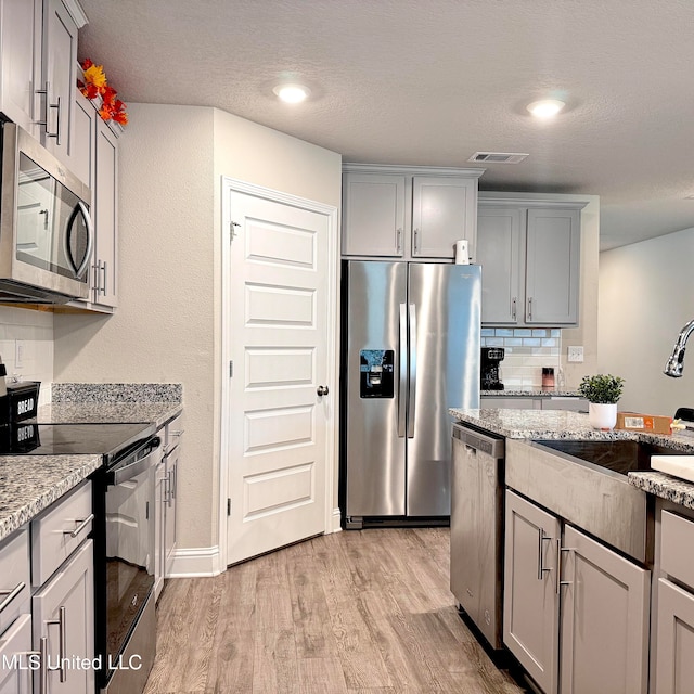 kitchen featuring stainless steel appliances, sink, light stone counters, gray cabinetry, and light wood-type flooring