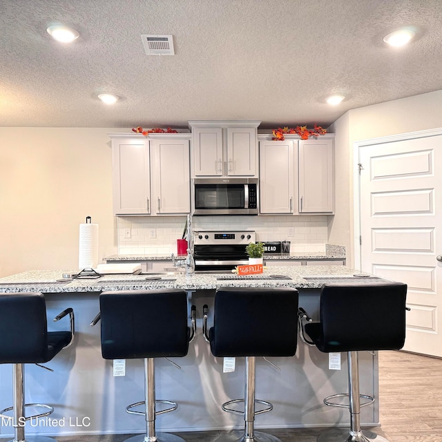 kitchen with stainless steel appliances, a breakfast bar area, backsplash, and light stone countertops