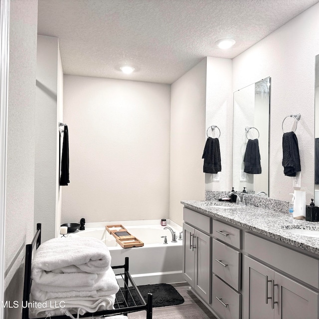 bathroom with a textured ceiling, vanity, a tub, and wood-type flooring