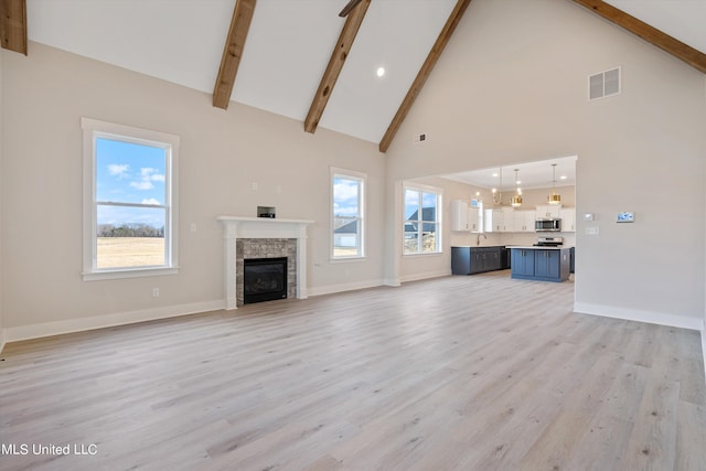 unfurnished living room featuring beam ceiling, high vaulted ceiling, light wood-type flooring, and a wealth of natural light