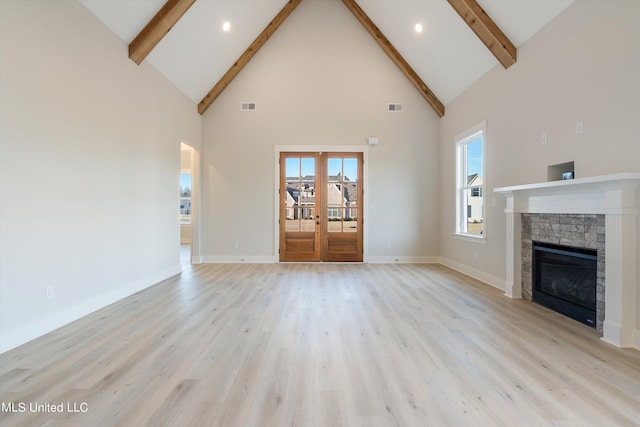 unfurnished living room with light wood-type flooring, french doors, a stone fireplace, beamed ceiling, and high vaulted ceiling