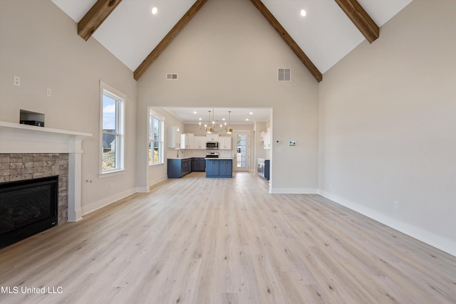 unfurnished living room featuring high vaulted ceiling, an inviting chandelier, light wood-type flooring, and a fireplace