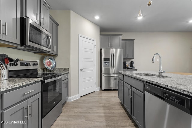 kitchen with appliances with stainless steel finishes, light stone countertops, a sink, gray cabinetry, and light wood-style floors