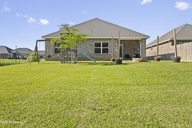 rear view of house with a lawn, roof with shingles, and fence