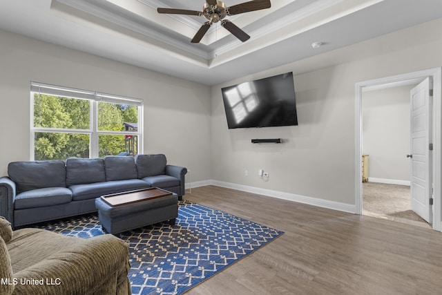 living room with crown molding, a raised ceiling, a ceiling fan, baseboards, and wood finished floors