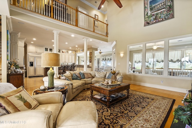 living room featuring a high ceiling, ornate columns, ornamental molding, light hardwood / wood-style floors, and ceiling fan