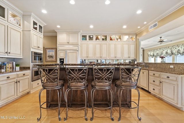 kitchen featuring stainless steel double oven, paneled refrigerator, dark stone counters, crown molding, and a breakfast bar