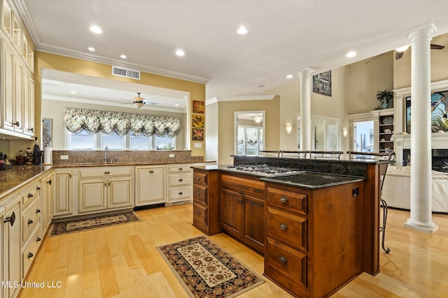 kitchen with cream cabinetry, stainless steel gas stovetop, dark stone countertops, crown molding, and light hardwood / wood-style flooring