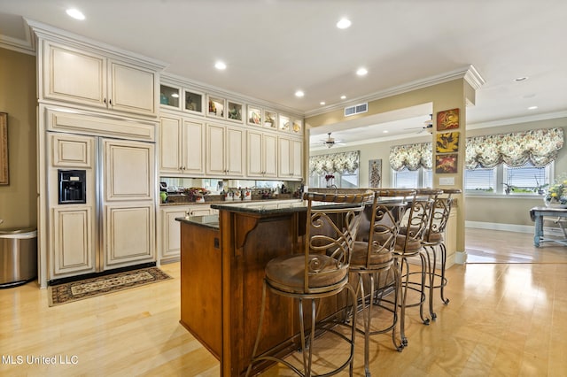 kitchen with cream cabinetry, dark stone countertops, a center island with sink, ornamental molding, and a breakfast bar