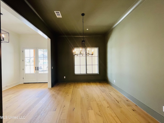 unfurnished dining area featuring an inviting chandelier, french doors, and light wood-type flooring