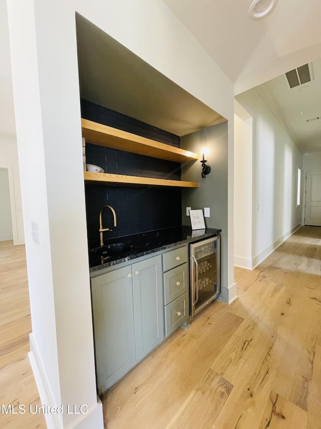 kitchen featuring dark stone countertops, sink, light hardwood / wood-style flooring, and beverage cooler