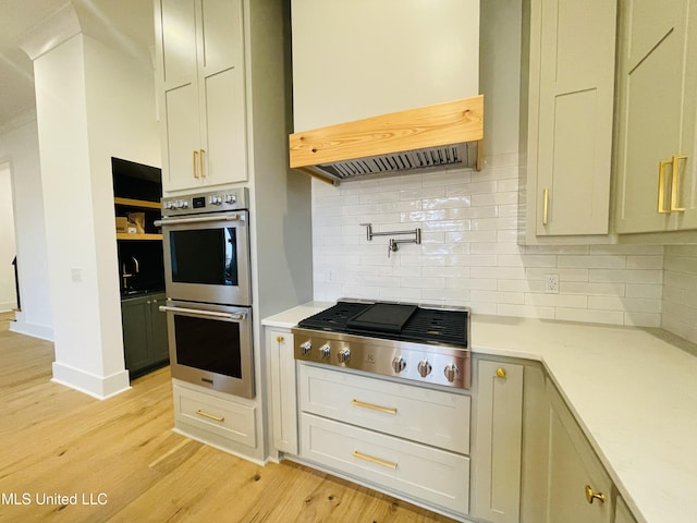 kitchen featuring decorative backsplash, appliances with stainless steel finishes, light hardwood / wood-style floors, and custom exhaust hood