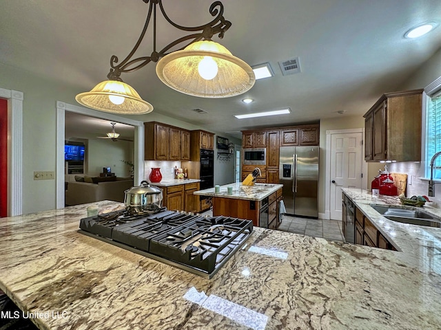 kitchen featuring black appliances, a kitchen island, backsplash, and light stone countertops