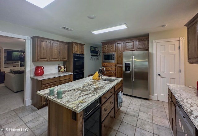 kitchen with stainless steel appliances, sink, a kitchen island with sink, backsplash, and light stone countertops