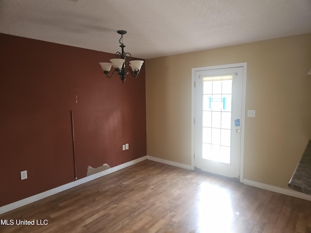 unfurnished dining area with hardwood / wood-style flooring, a textured ceiling, and a chandelier