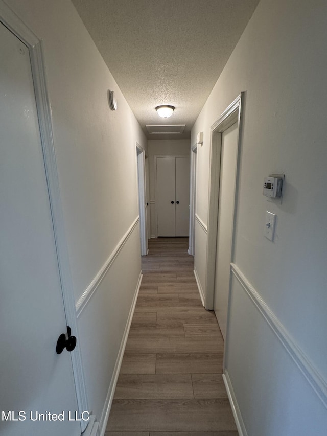 corridor with light wood-type flooring and a textured ceiling