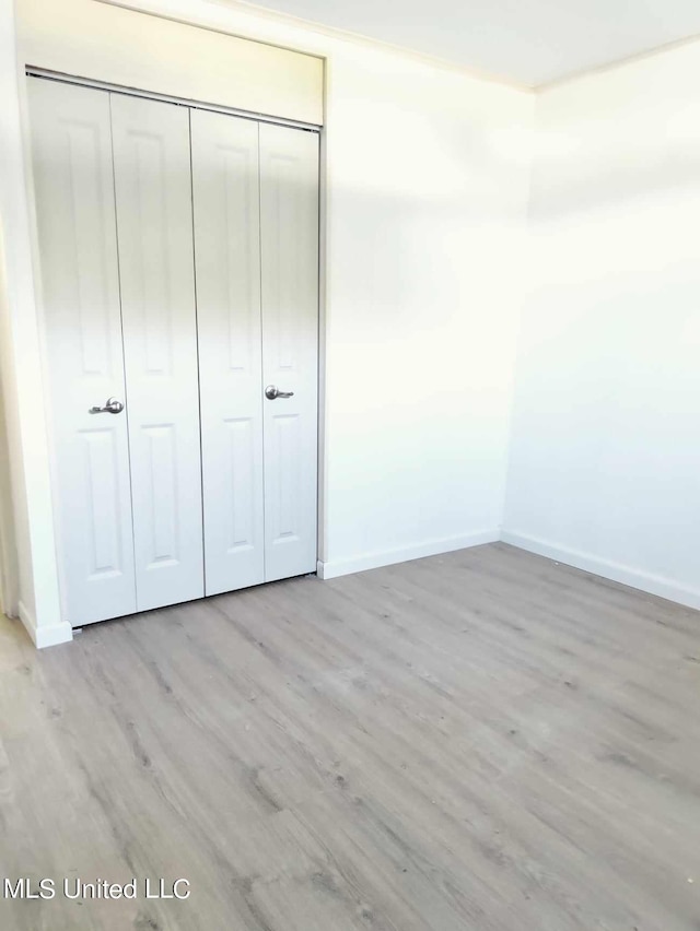 unfurnished bedroom featuring a closet, light wood-type flooring, and baseboards