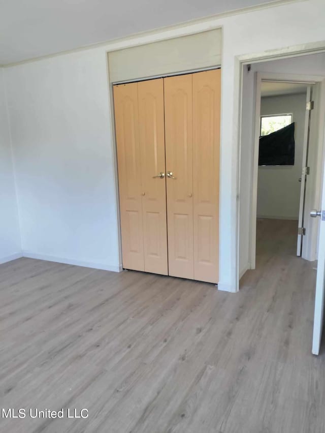 unfurnished bedroom with light wood-type flooring, baseboards, and a closet