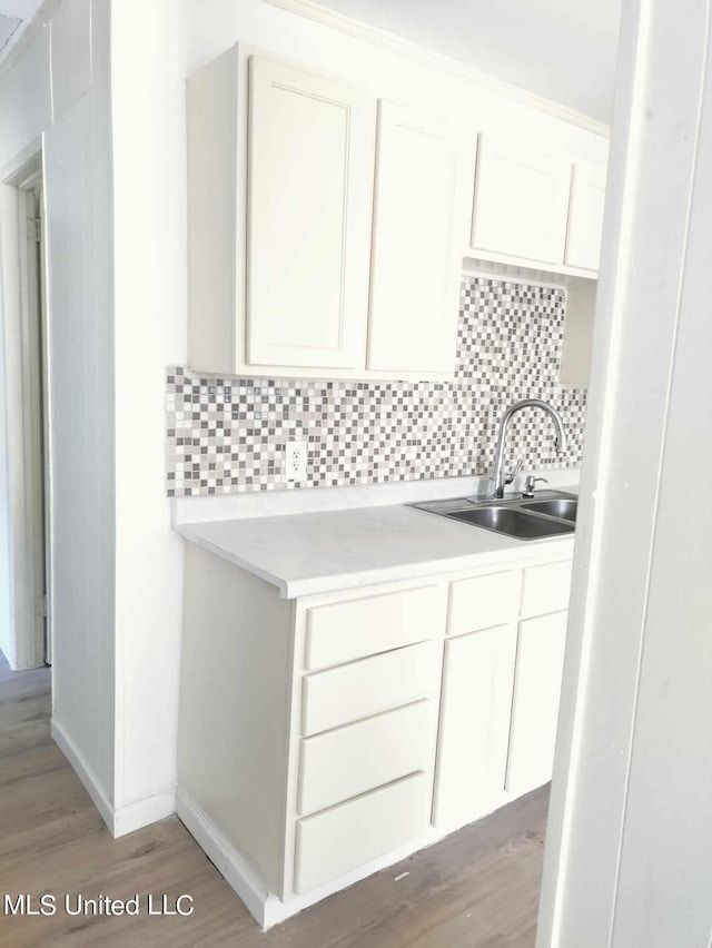 kitchen featuring a sink, white cabinetry, light wood-style floors, light countertops, and tasteful backsplash