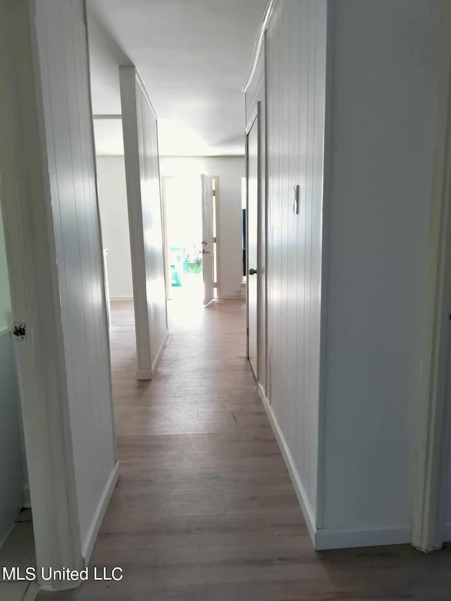 hall featuring wood walls, light wood-style flooring, and baseboards