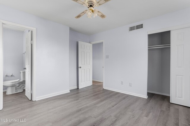 unfurnished bedroom featuring a closet, ensuite bathroom, light wood-type flooring, and ceiling fan