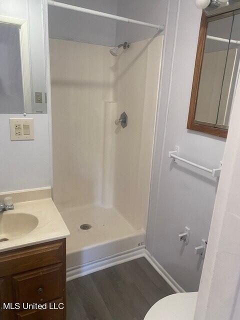 bathroom featuring vanity, toilet, wood-type flooring, and a shower