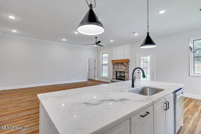 kitchen featuring a center island with sink, sink, white cabinetry, light stone countertops, and light hardwood / wood-style flooring