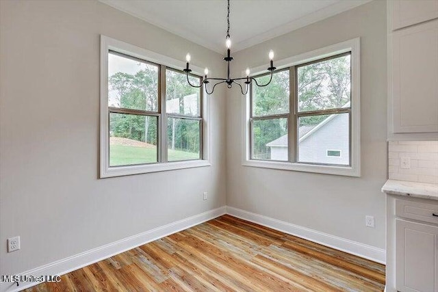 unfurnished dining area with ornamental molding, light wood-type flooring, a wealth of natural light, and a chandelier