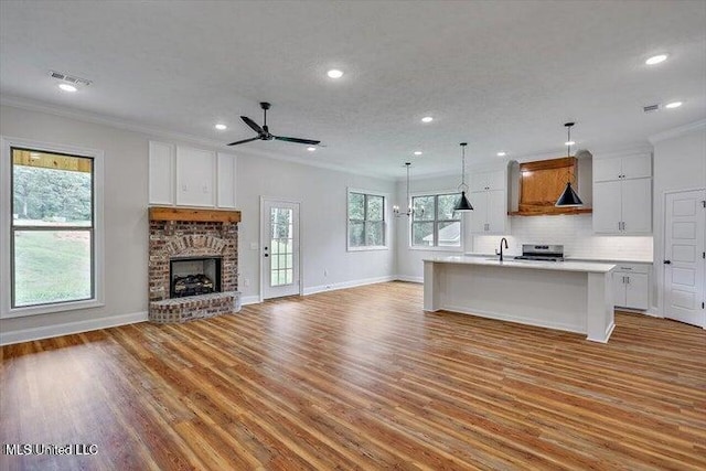 kitchen featuring a fireplace, a kitchen island with sink, white cabinetry, and light wood-type flooring