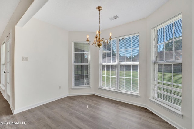 unfurnished dining area with an inviting chandelier, a textured ceiling, and wood-type flooring