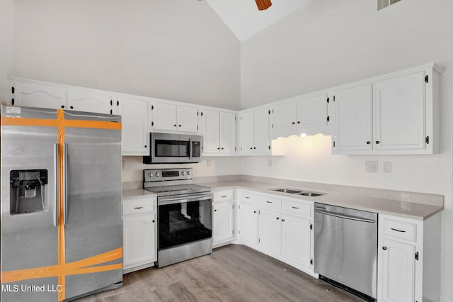 kitchen with light hardwood / wood-style flooring, stainless steel appliances, sink, white cabinetry, and high vaulted ceiling